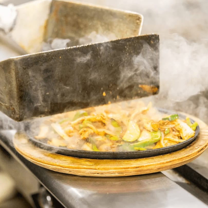 Sizzling fajitas with chicken, onions, and bell peppers on a hot cast iron plate.